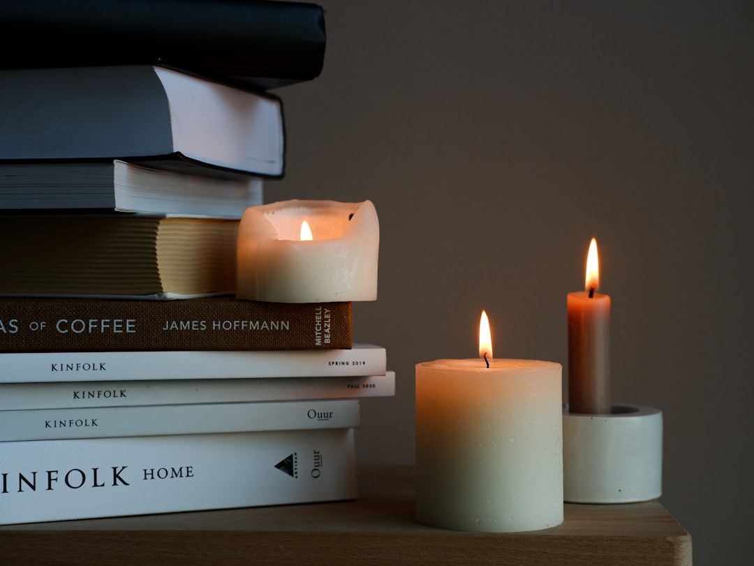 Luxury candles displayed on wooden bookshelf with design books and plants